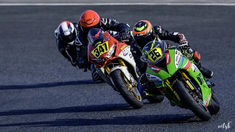 Deux pilotes sur des motos verte et orange en lutte rapprochée