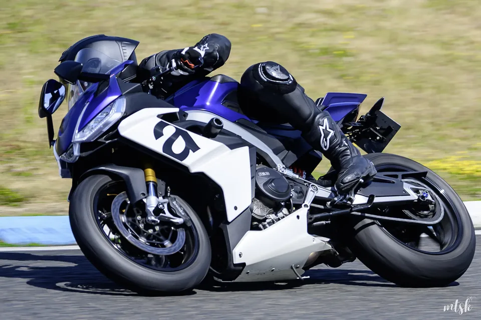 Moto blanche et bleue suivie au téléobjectif dans une courbe