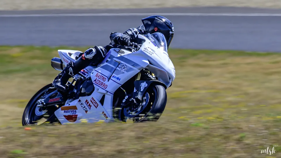 Moto bleue et blanche inclinée dans une courbe en bord de piste