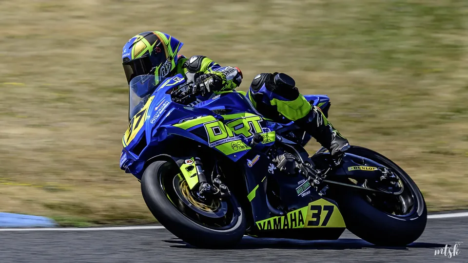 Moto bleue et jaune vue de trois quarts arrière pendant une relance en sortie de courbe