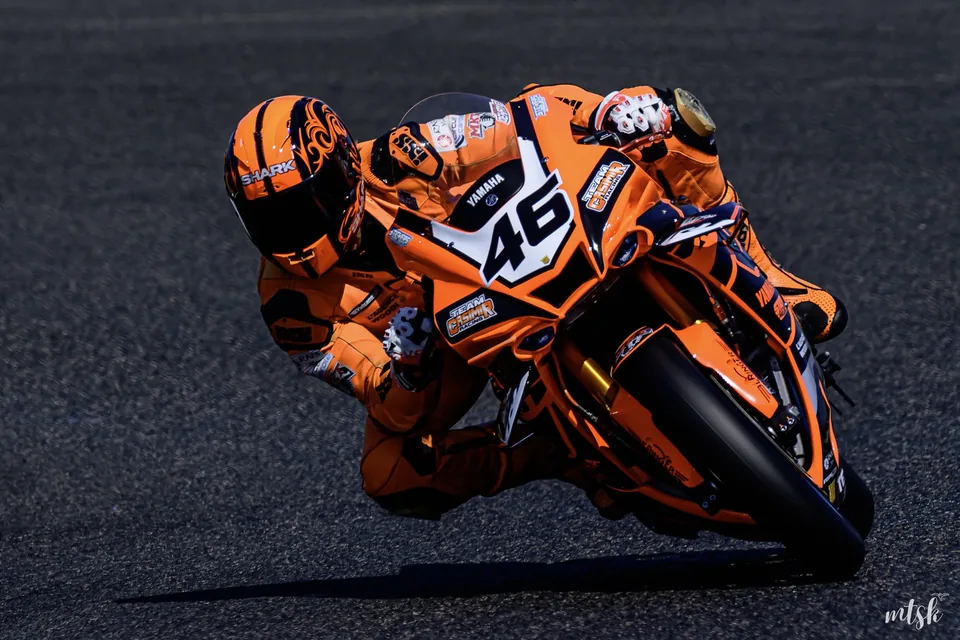 Moto orange très inclinée avec le pilote déhanché dans le virage