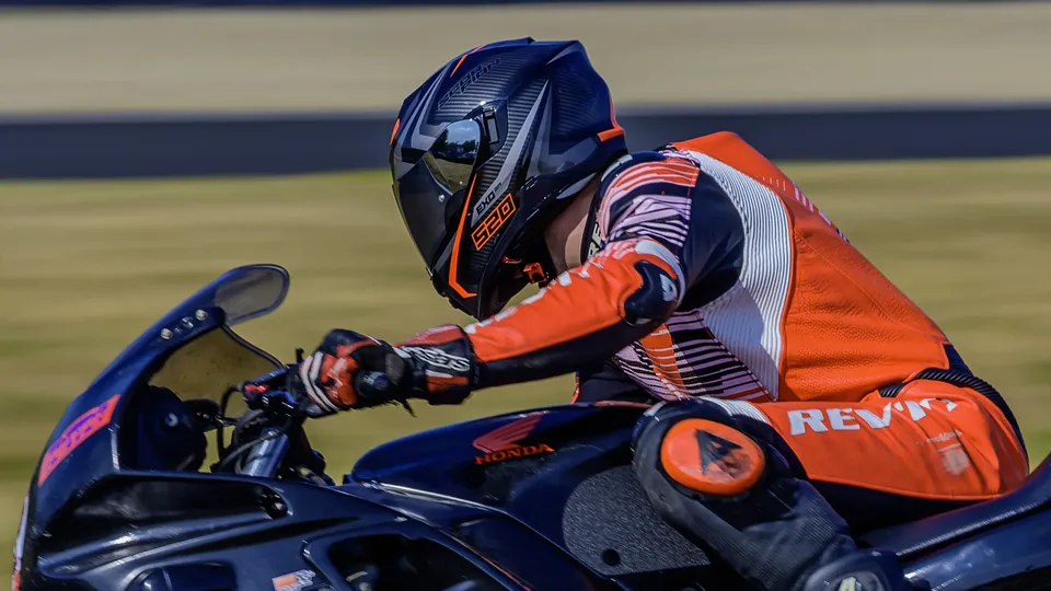 Pilote en combinaison orange concentré au guidon de sa moto