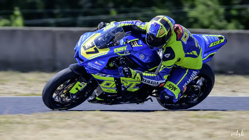 Pilote sur une moto bleue et jaune photographié en forte inclinaison sur circuit